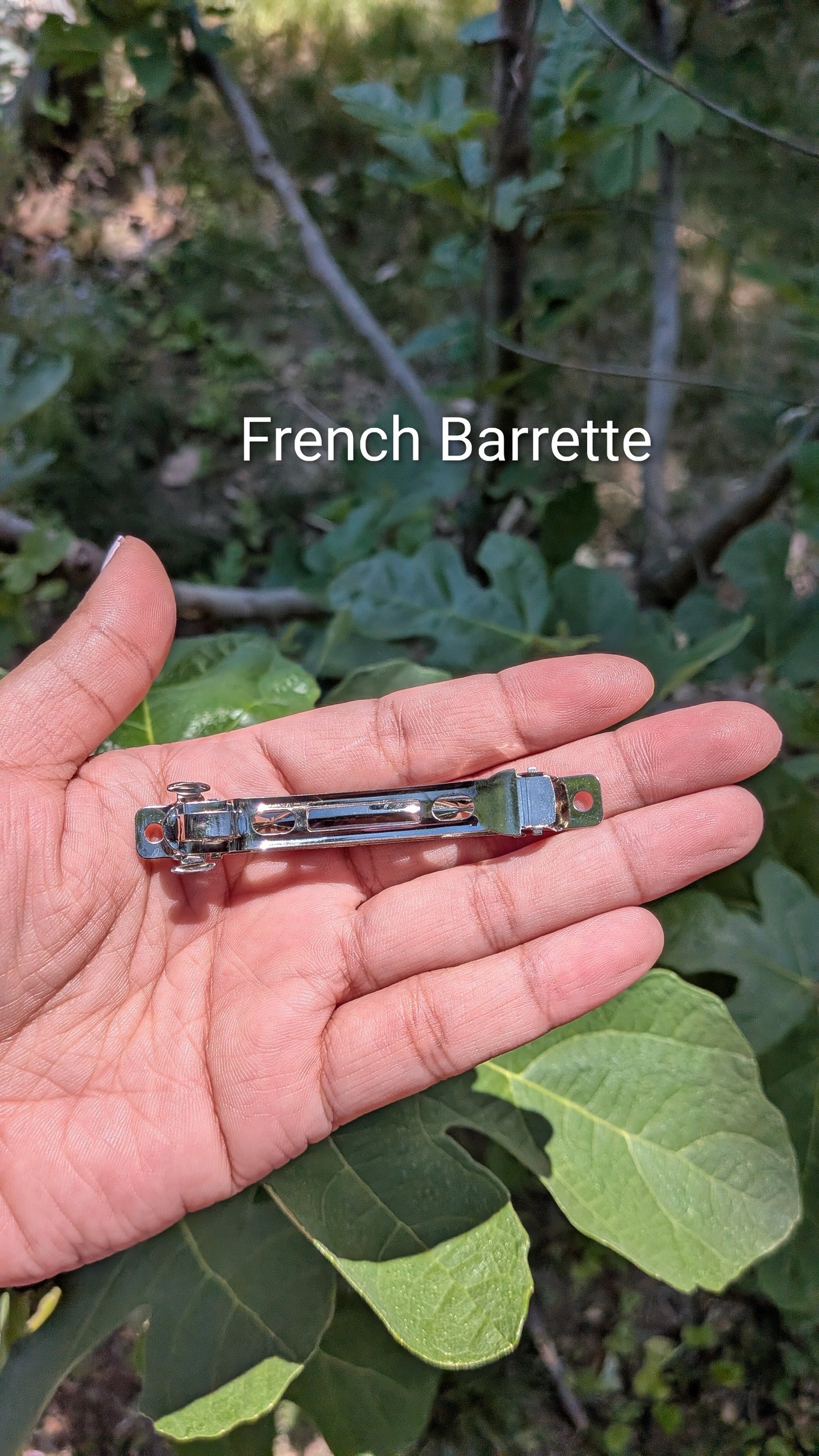 Hand holding a French barrette with green foliage in the background