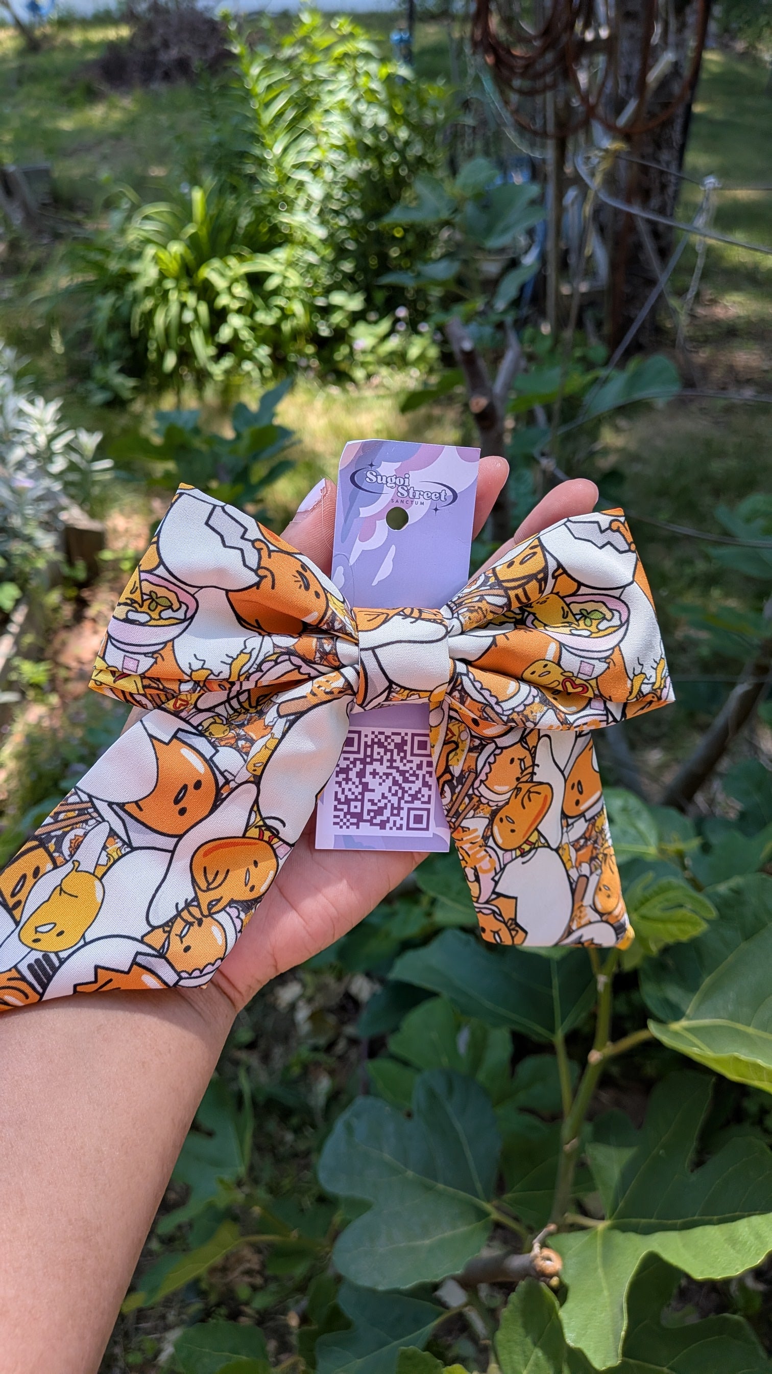 Hair bow with gudetama design held in front of a natural background