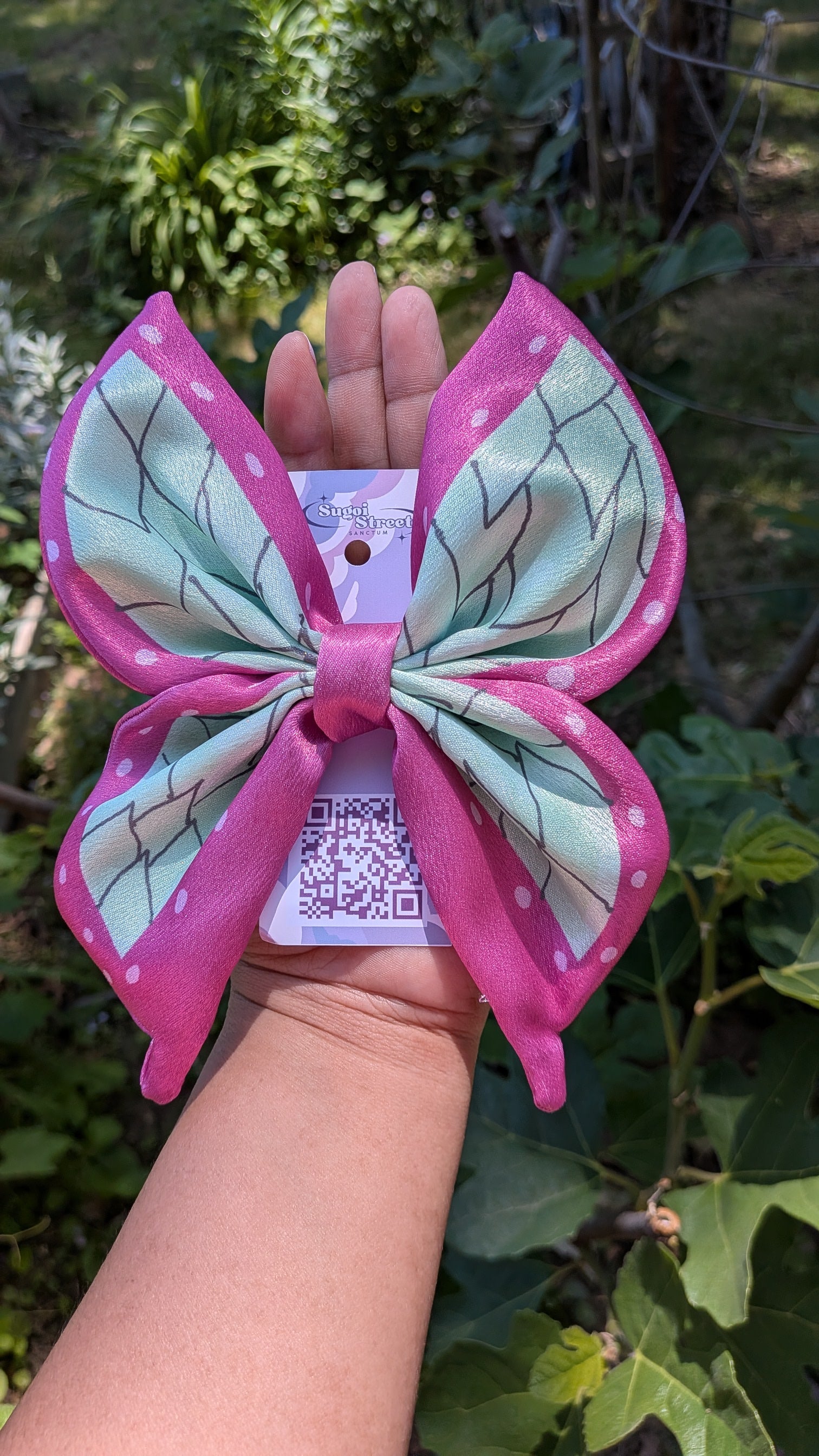 Pink and green butterfly-shaped hair bow held by a hand with a blurred natural background