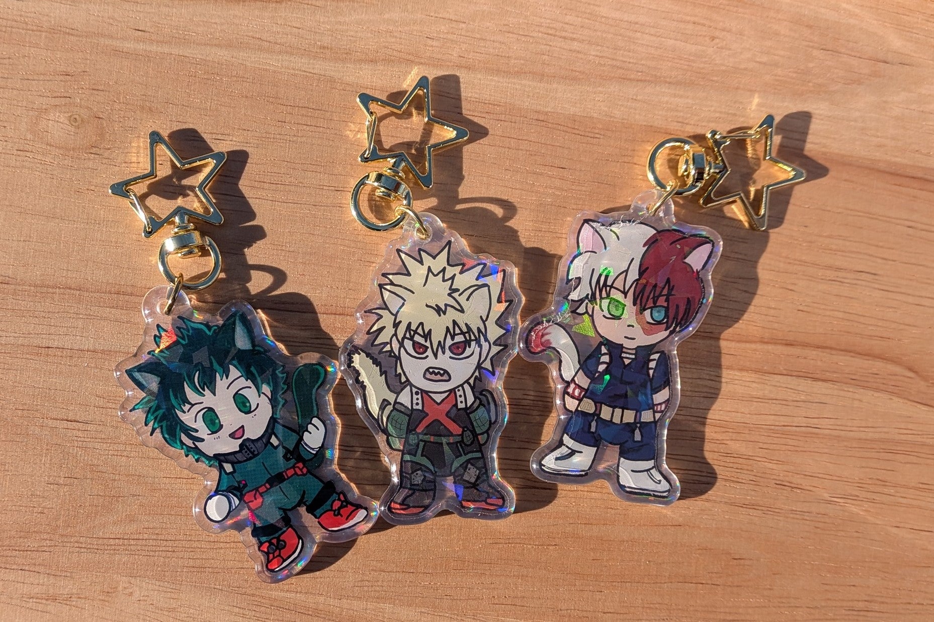 Three cartoon character keychains of the three musketeers from My Hero Academia on a wooden surface