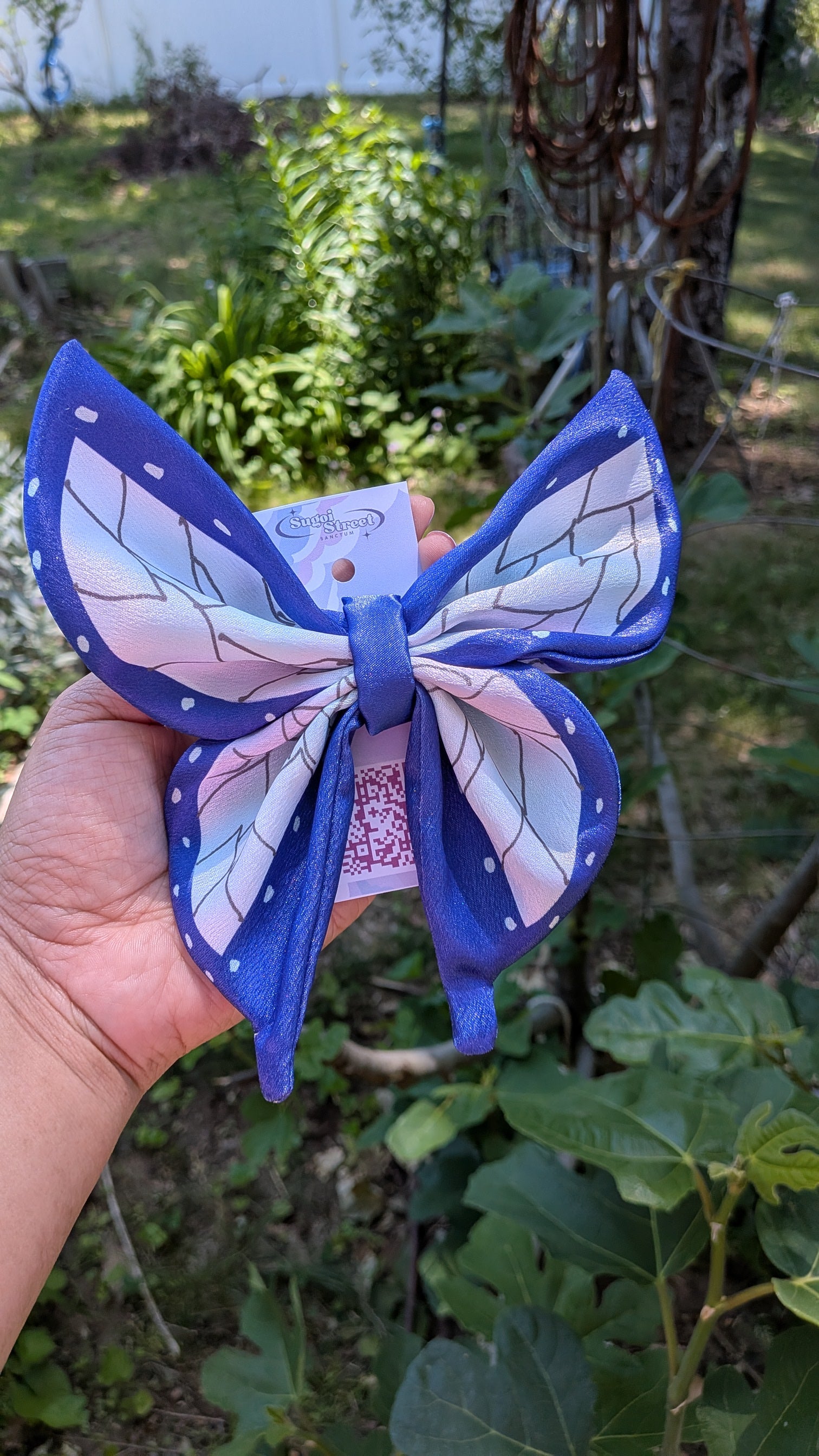 Blue butterfly-shaped hair clip held in a hand with a garden background