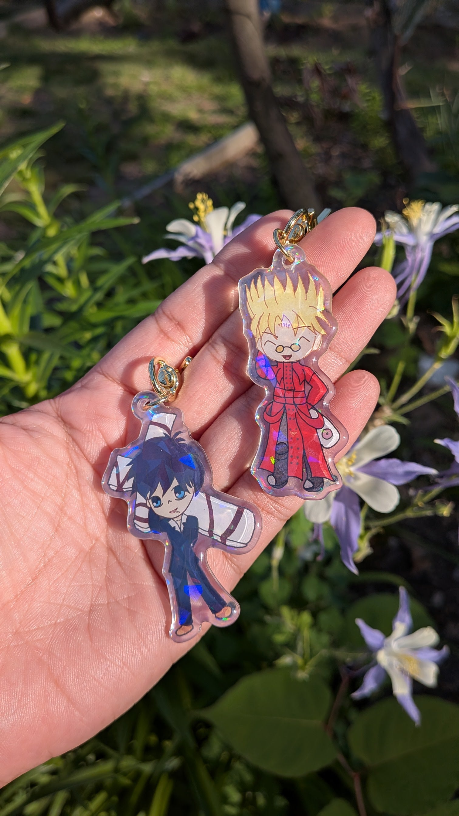 Two colorful keychains of Vash Stampede and Nicholas D. Wolfwood held in a hand with a natural background