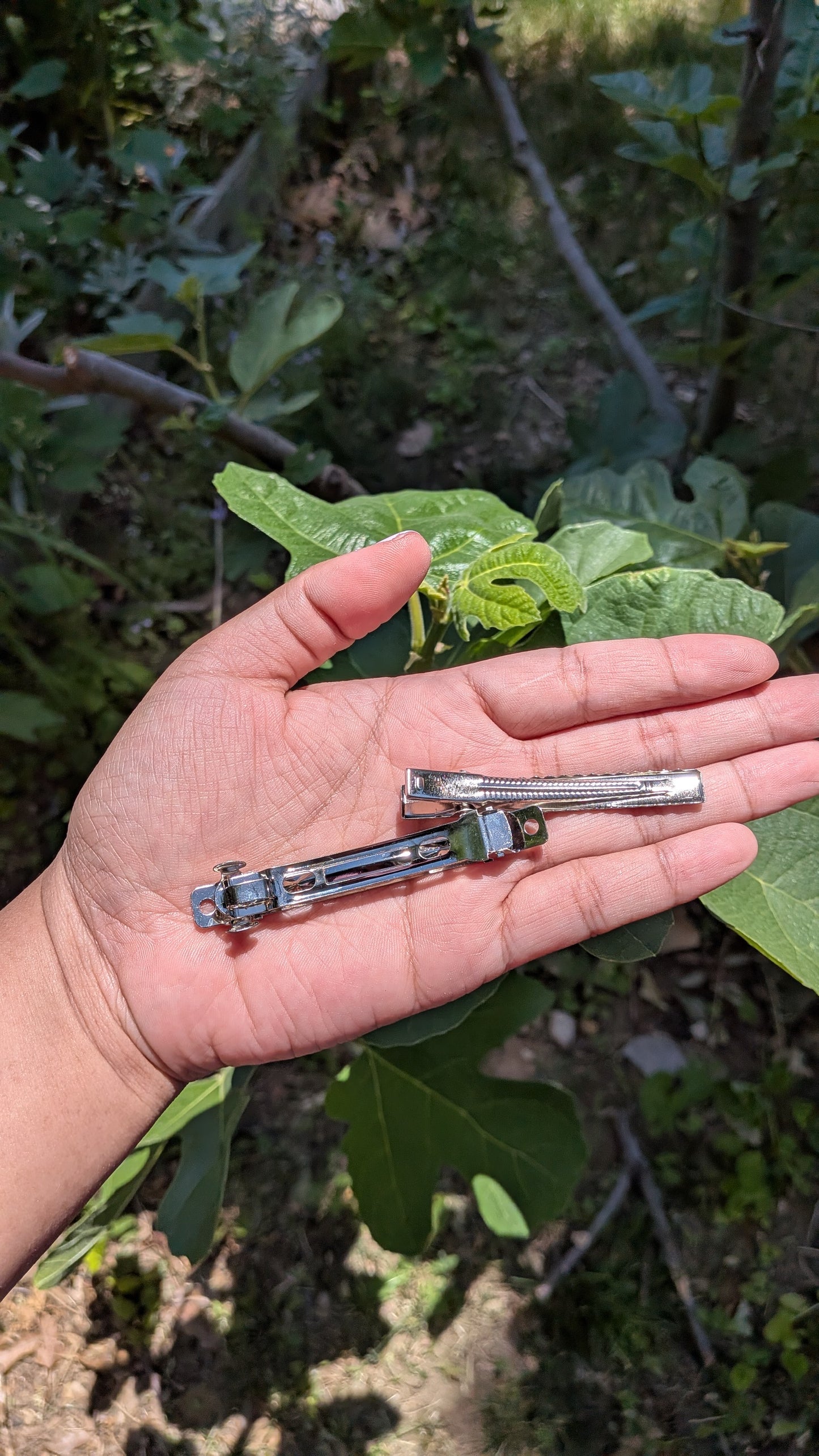 Hand holding two small metal objects against a natural background with green leaves.
