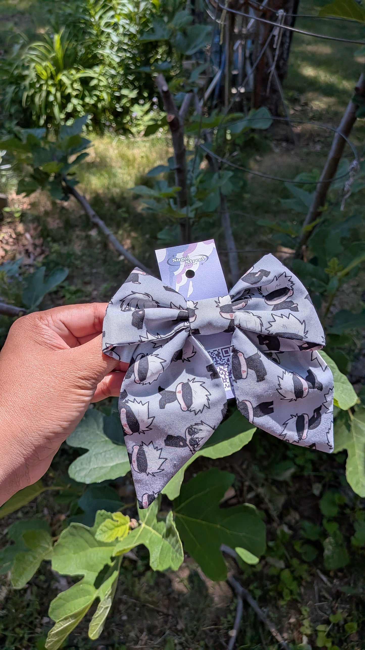 Gray bow with a gojo jjk pattern held in front of green foliage