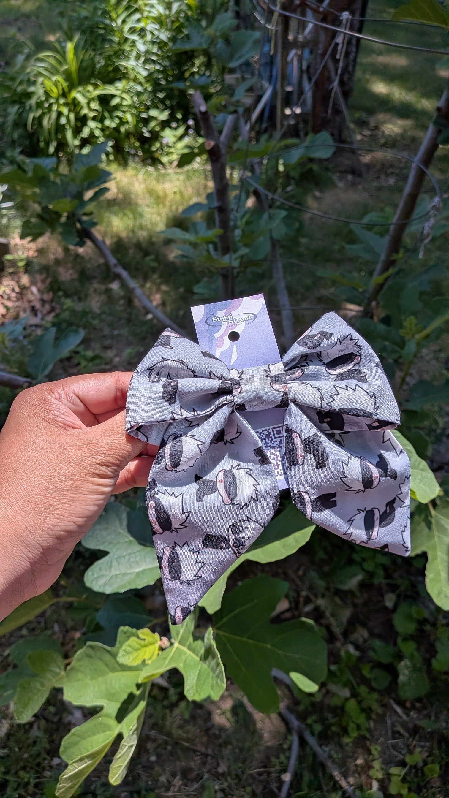 Gray bow with a gojo jjk pattern held in front of green foliage