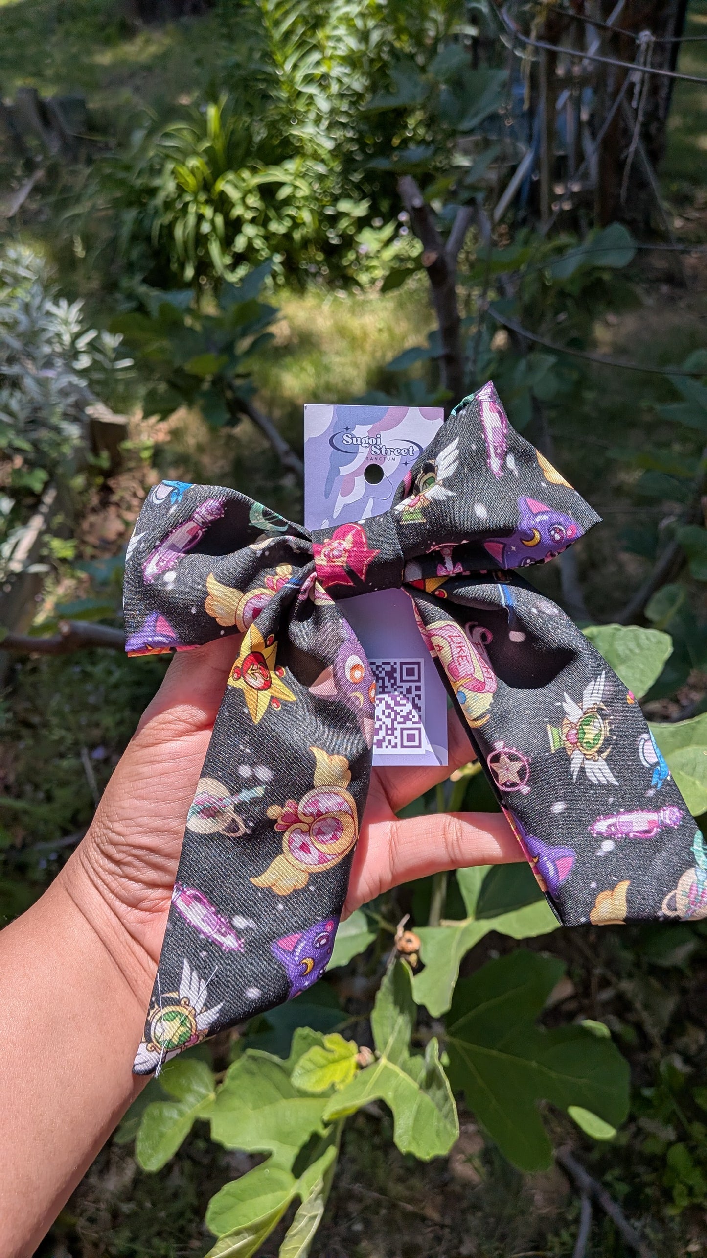 Decorative bow with sailor moon pattern held by a hand against a natural background