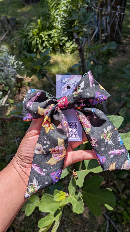 Decorative bow with sailor moon pattern held by a hand against a natural background